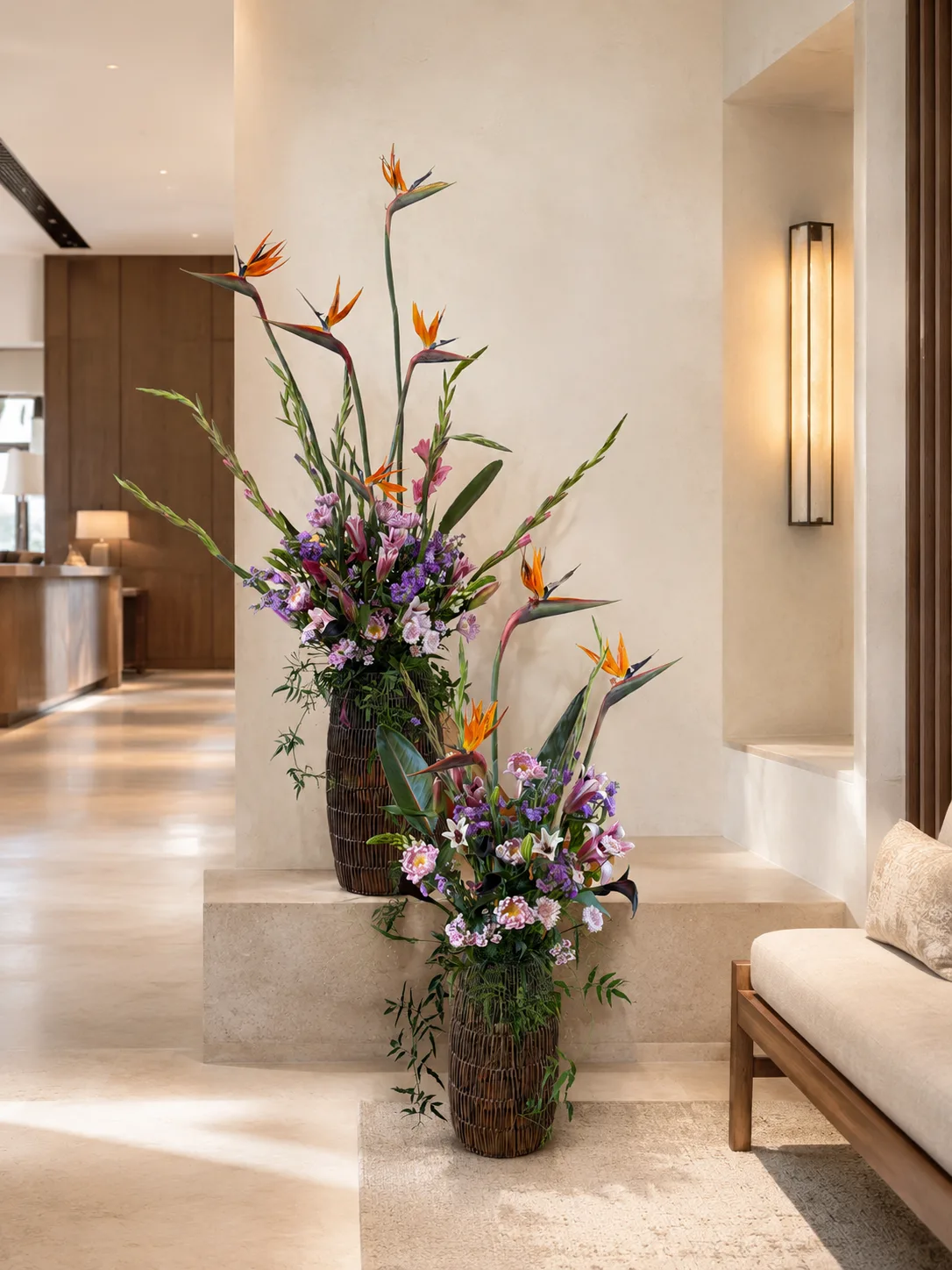 Bird of paradise and purple gladiolus arrangement in woven vases on a lobby staircase beside a wall sconce