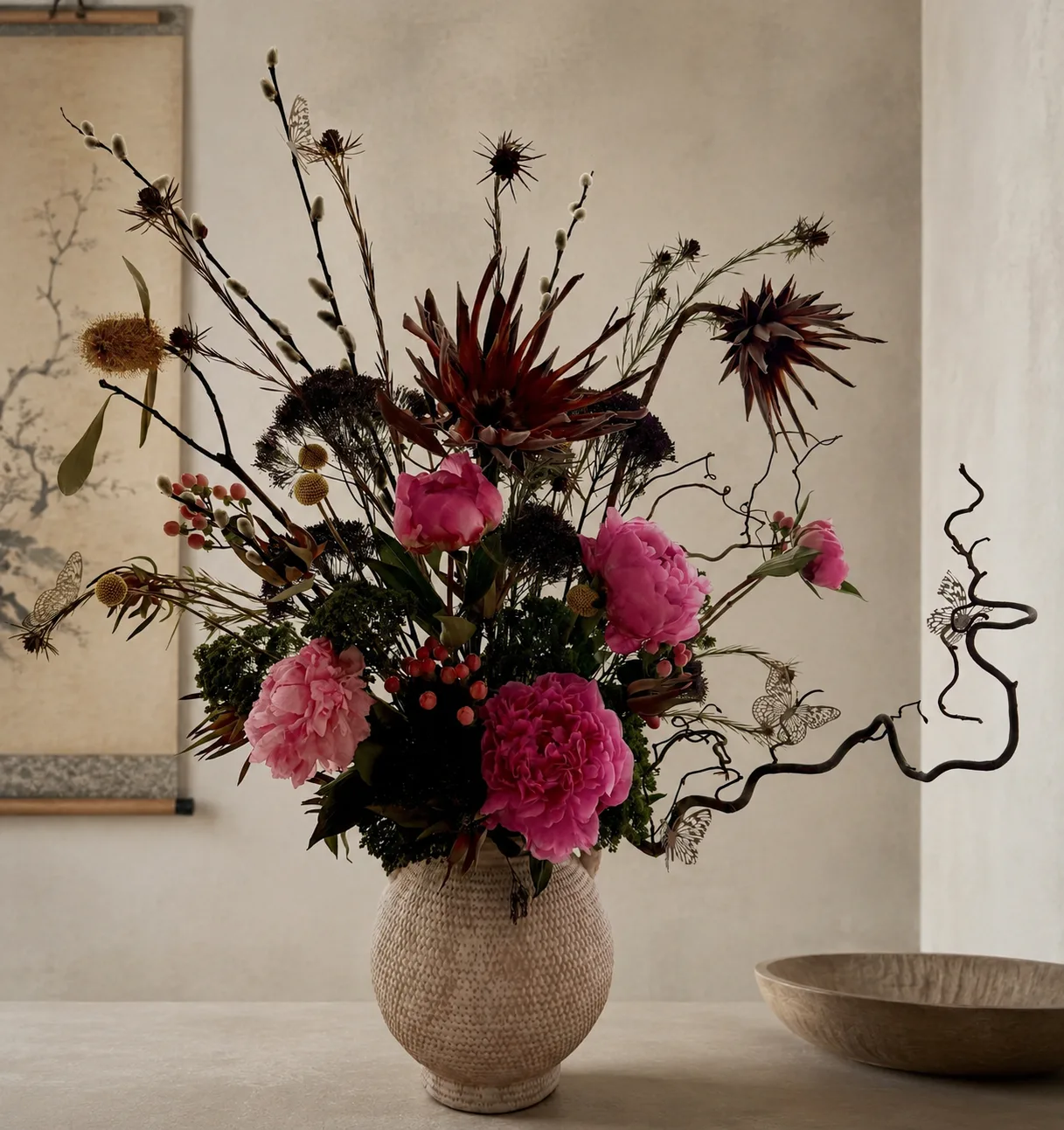 Pink peony and dried thistle arrangement with willow branches and paper butterfly accents against a Japanese scroll