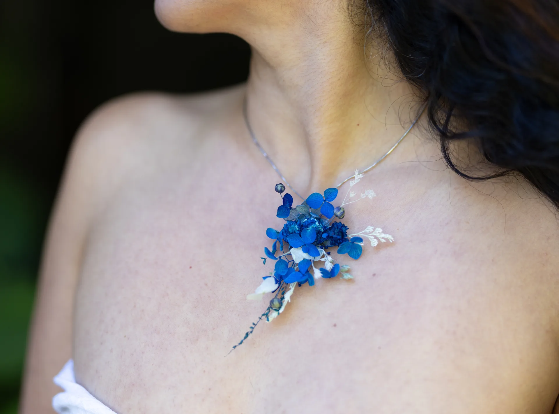 Dried blue hydrangea pendant necklace resting on a bare collarbone