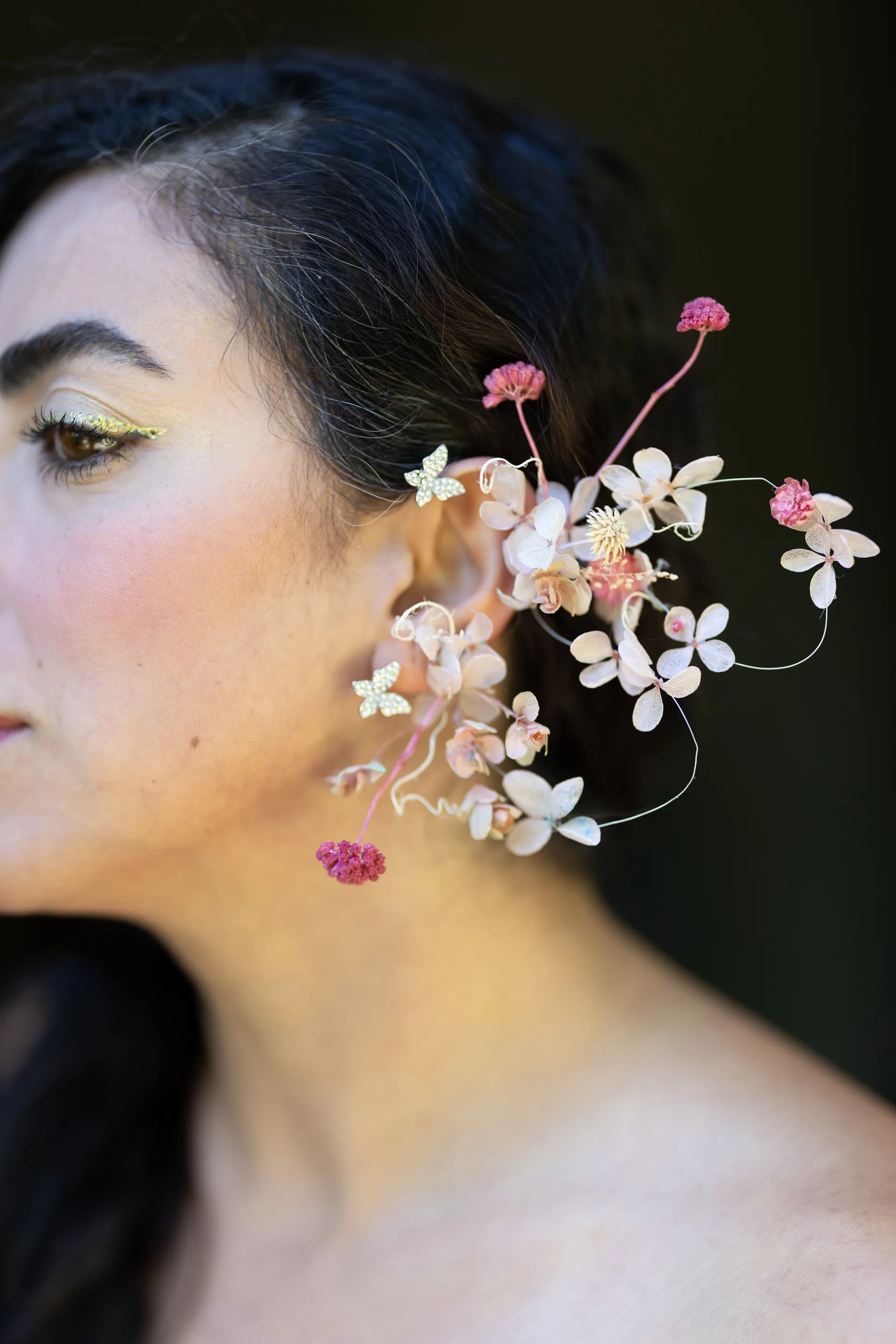 Profile close-up of an elaborate dried flower ear cuff with cream blossoms and pink accents cascading from the ear