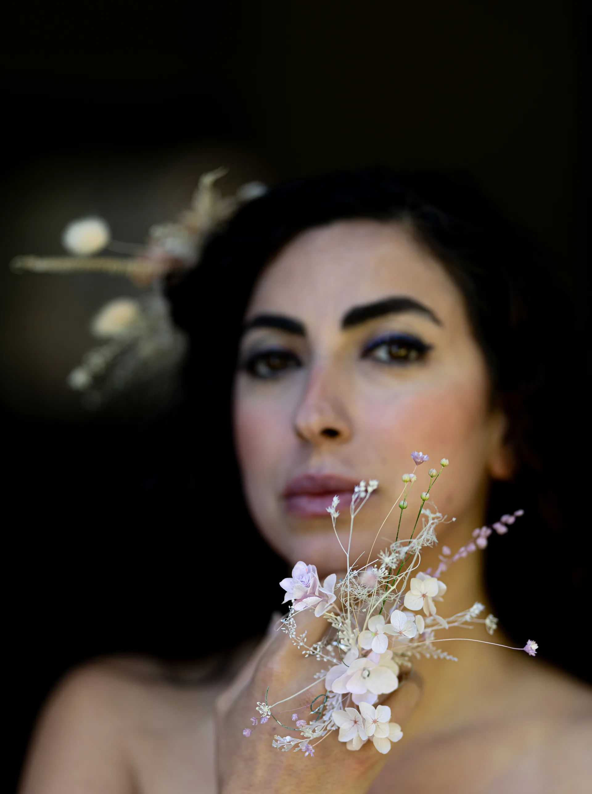 Close-up portrait of a model with a dried hydrangea and baby's breath necklace cascading over her collarbone, a matching dried flower hairpiece behind her