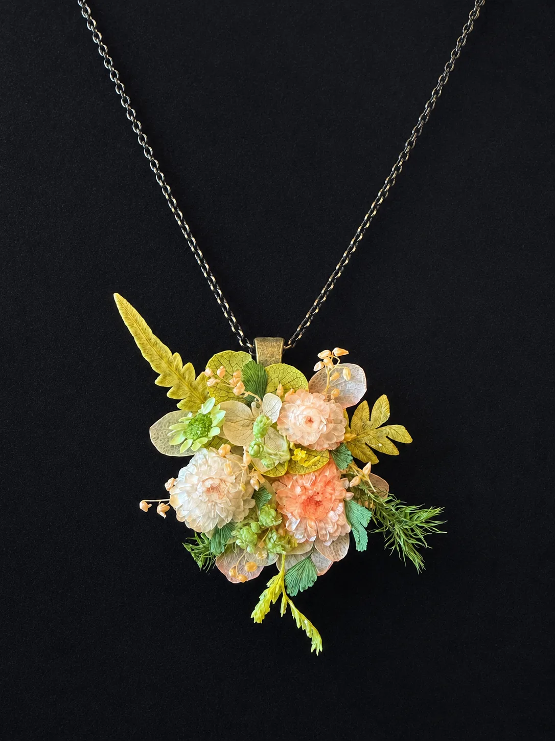 Pressed flower cluster pendant necklace in clear resin, on a fine chain against a black background
