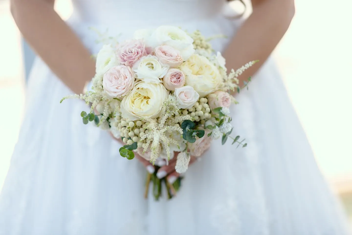 Close-up of a bride holding a blush and ivory garden rose bouquet with astilbe and eucalyptus